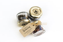 Three small glass jars with tea leaves, each labeled with a tag, on a white background. Lulu Island Honey